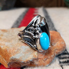 Navajo silver ring featuring a dark bear claw, oval turquoise stone, and detailed feather, scroll, and bead-style silverwork in an elongated statement design; side view.