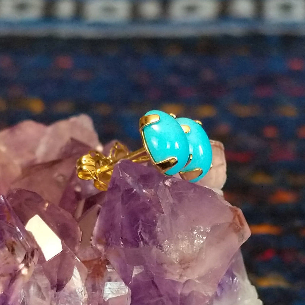 Two Navajo turquoise cabochon earrings with blue stones set in gold settings.