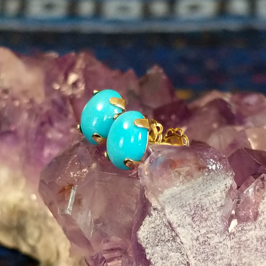 Two Navajo turquoise cabochon earrings with blue stones set in gold settings.