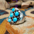 Sterling silver Navajo turquoise cluster ring featuring seven turquoise cabochons, serrated bezels, silver raindrop accents, and a classic Southwestern floral cluster design; side view.