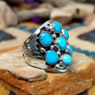 Sterling silver Navajo turquoise cluster ring featuring seven turquoise cabochons, serrated bezels, silver raindrop accents, and a classic Southwestern floral cluster design; side view.