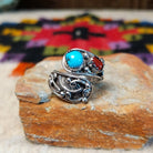 This eye-catching Navajo Turquoise & Coral Feather Ring features turquoise and red coral stones in sawtooth silver bezels with detailed feather, scroll, and silver bead accents.