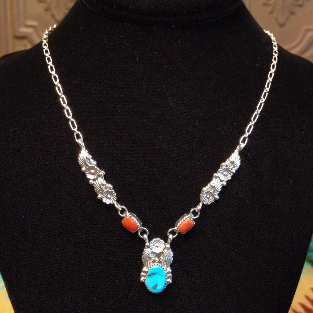 Turquoise and coral set in notched bezels with intricate feather and floral detailing on a sterling silver chain.