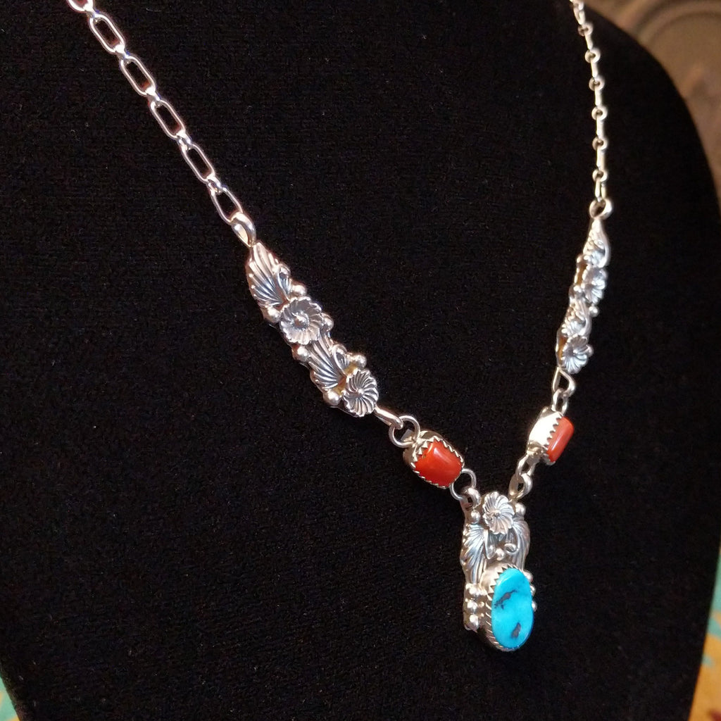 Turquoise and coral set in notched bezels with intricate feather and floral detailing on a sterling silver chain.