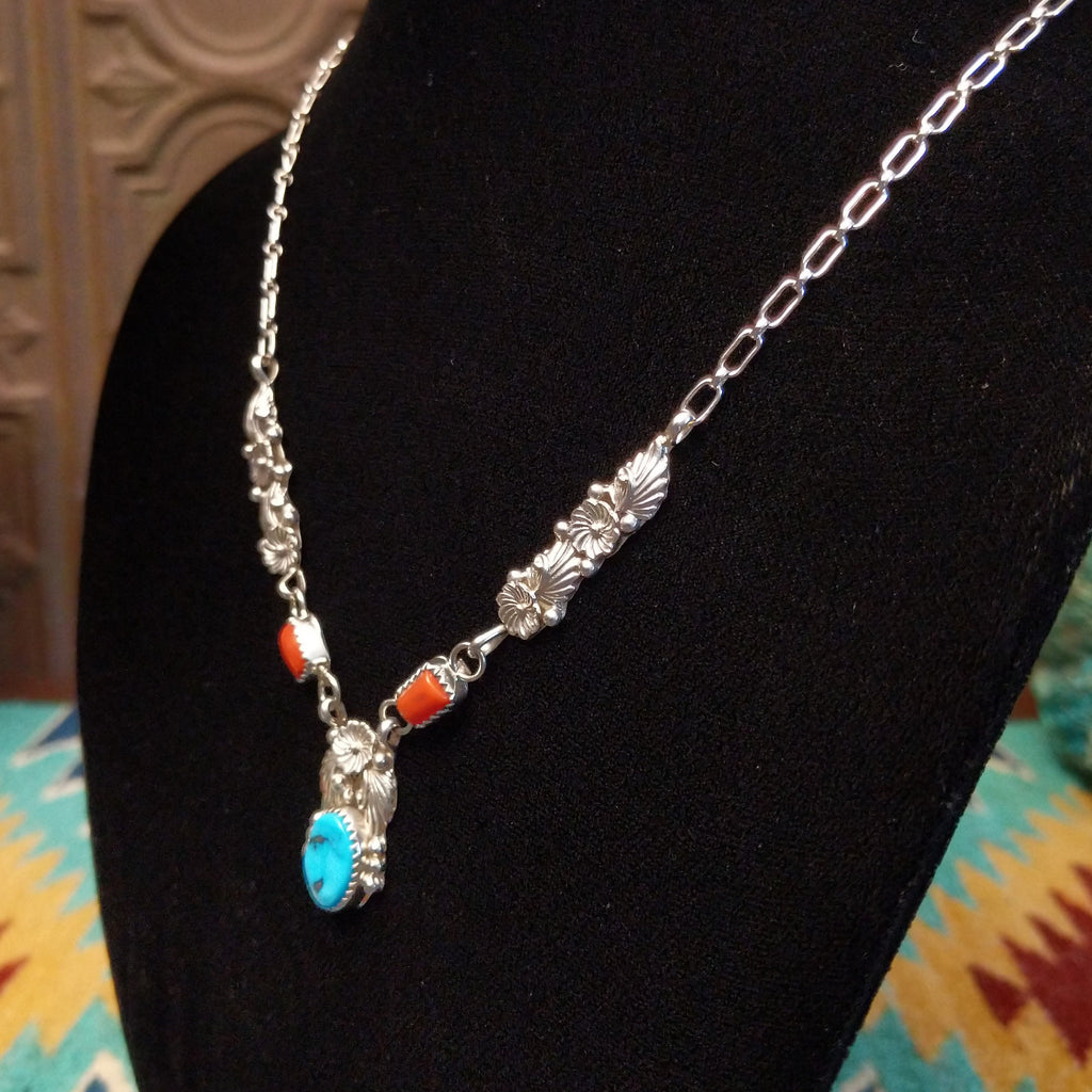 Turquoise and coral set in notched bezels with intricate feather and floral detailing on a sterling silver chain.