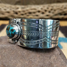 Navajo turquoise cuff by L.T.C., featuring an oval blue turquoise stone with natural black matrix set in a handcrafted sterling silver cuff with hand-stamped details, decorative silver accents, and a twisted rope bezel; side view.