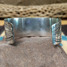 Navajo turquoise cuff by L.T.C., featuring an oval blue turquoise stone with natural black matrix set in a handcrafted sterling silver cuff with hand-stamped details, decorative silver accents, and a twisted rope bezel; underside view.