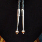 Navajo Turquoise Flower Bolo Tie by M. featuring an openwork silver flower with a round turquoise center stone, braided black leather cord, and polished silver tips; tips view.