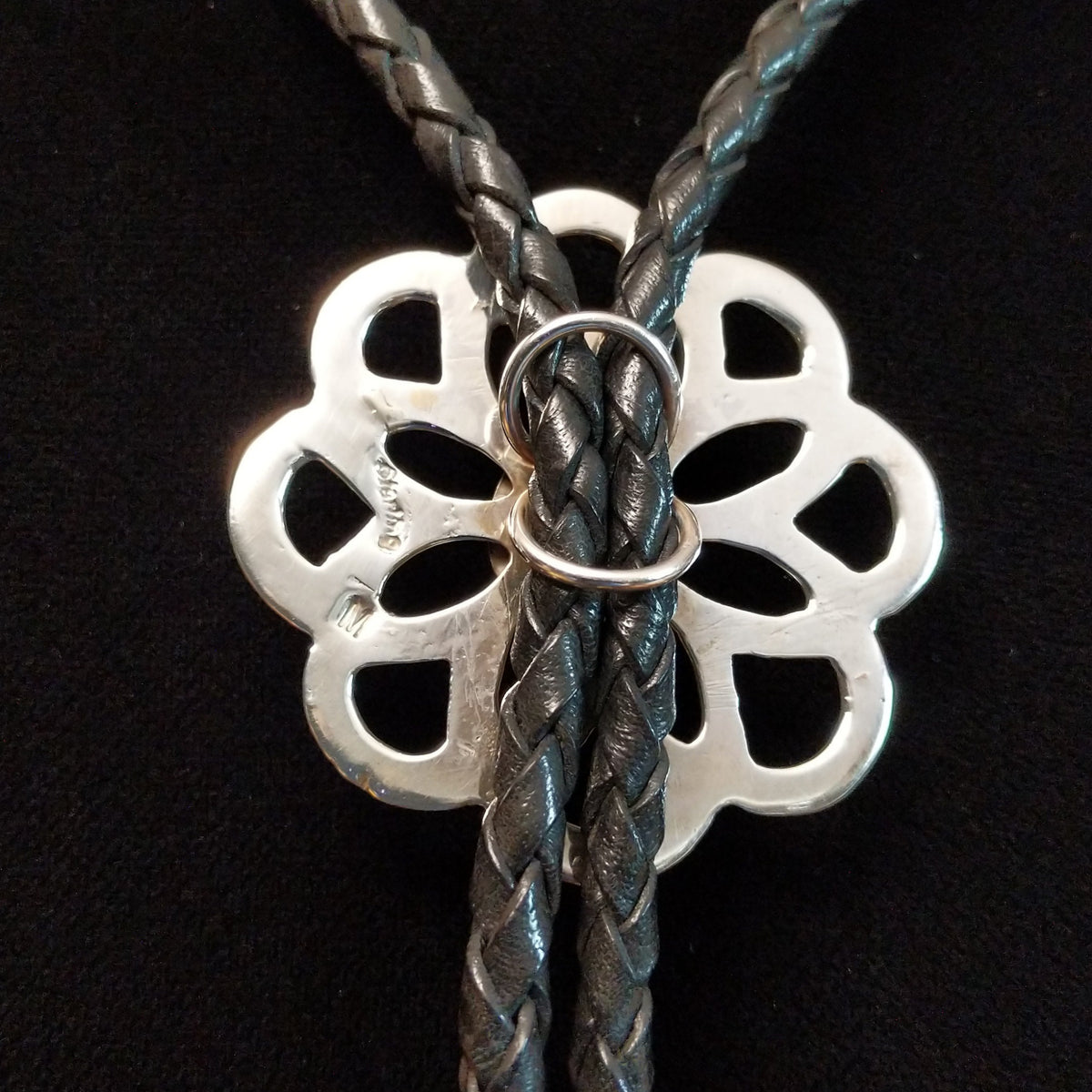 Navajo Turquoise Flower Bolo Tie by M. featuring an openwork silver flower with a round turquoise center stone, braided black leather cord, and polished silver tips; backside view with artist and Sterling Silver stamp.