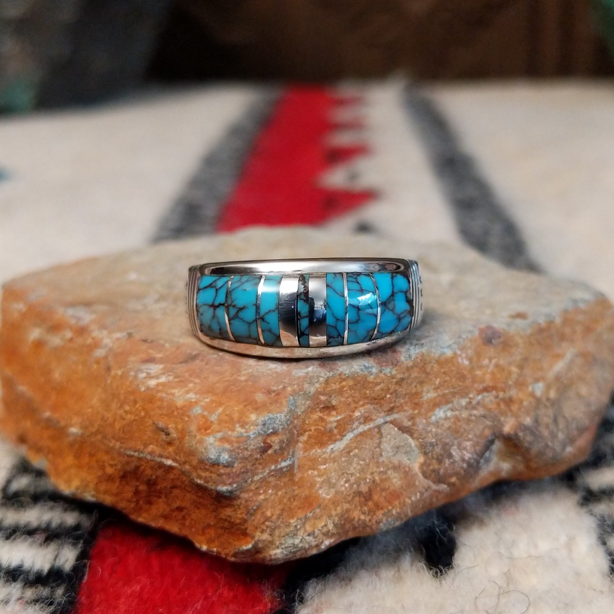 Navajo turquoise inlay ring featuring bright blue turquoise with dark matrix, segmented by polished silver channels across a wide silver band.