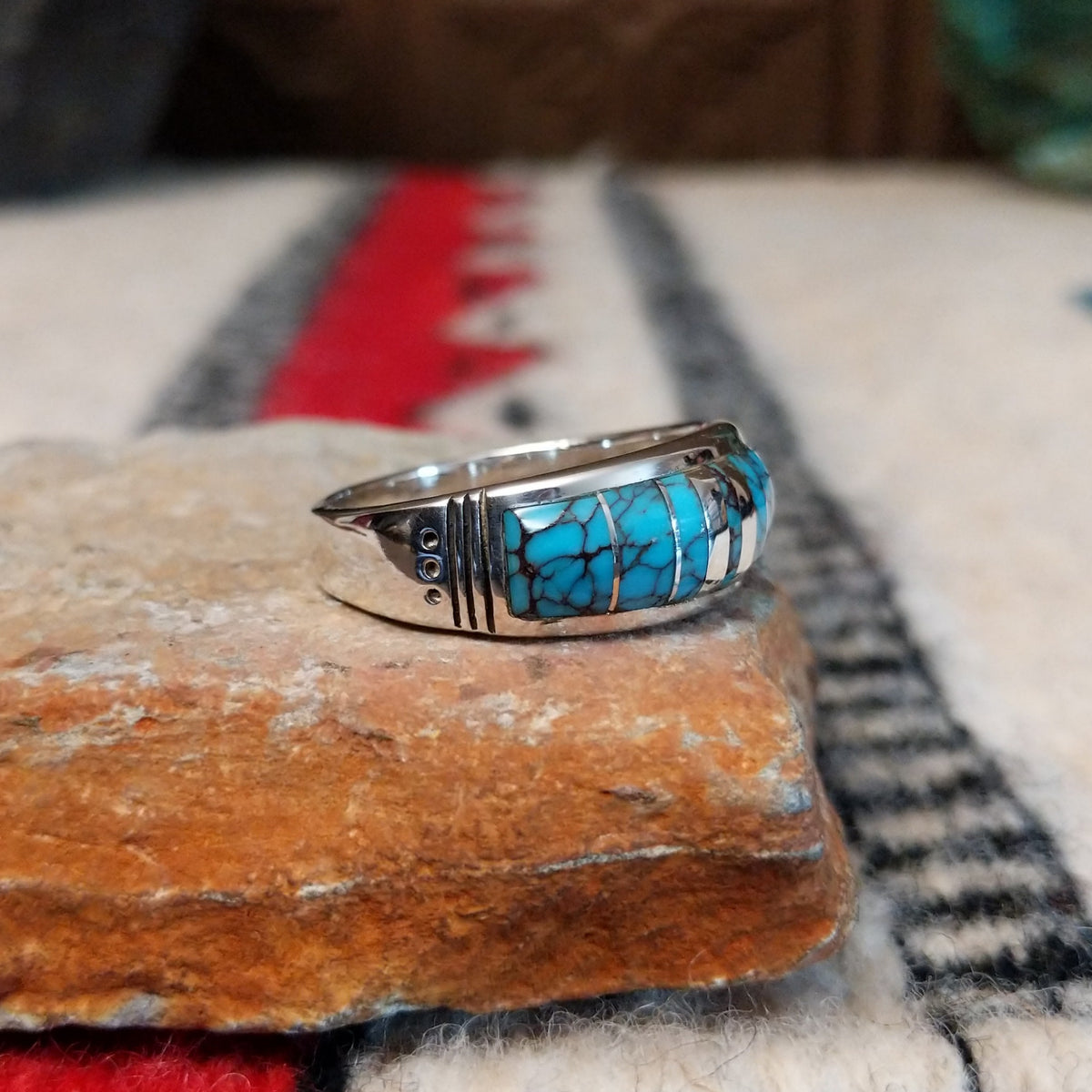 Navajo turquoise inlay ring featuring bright blue turquoise with dark matrix, segmented by polished silver channels across a wide silver band; side view.