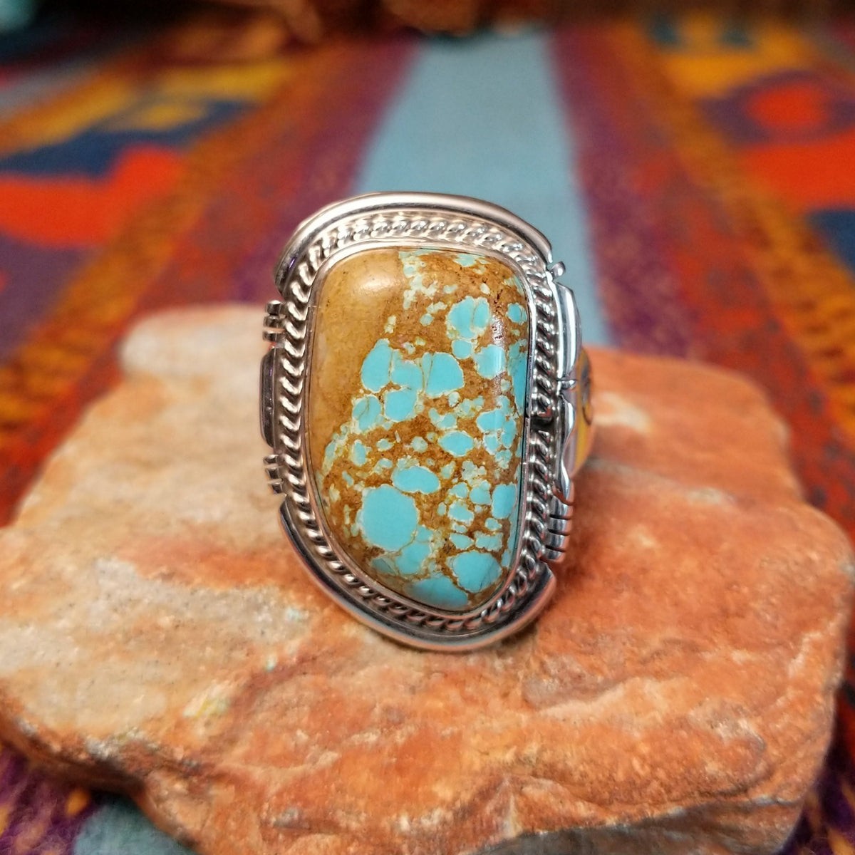 Navajo Turquoise Mountain Turquoise Ring by S.N. featuring a large rounded rectangular turquoise stone with golden-brown matrix, framed by detailed twisted-rope and decorative silverwork.