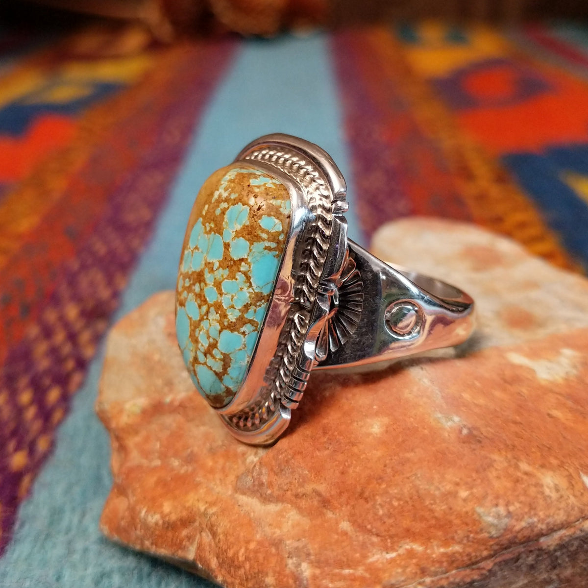 Navajo Turquoise Mountain Turquoise Ring by S.N. featuring a large rounded rectangular turquoise stone with golden-brown matrix, framed by detailed twisted-rope and decorative silverwork; side view.