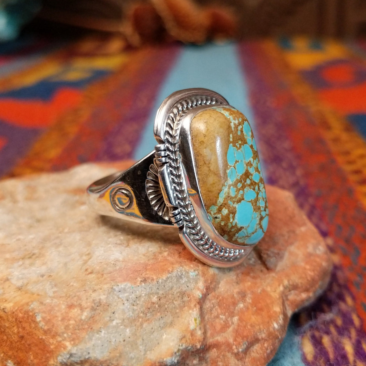 Navajo Turquoise Mountain Turquoise Ring by S.N. featuring a large rounded rectangular turquoise stone with golden-brown matrix, framed by detailed twisted-rope and decorative silverwork; side view.