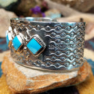 Handcrafted Navajo sterling silver cuff featuring five diamond-shaped turquoise stones in twisted rope bezels with intricate hand-stamped Southwestern designs and silver bead accents; side view.