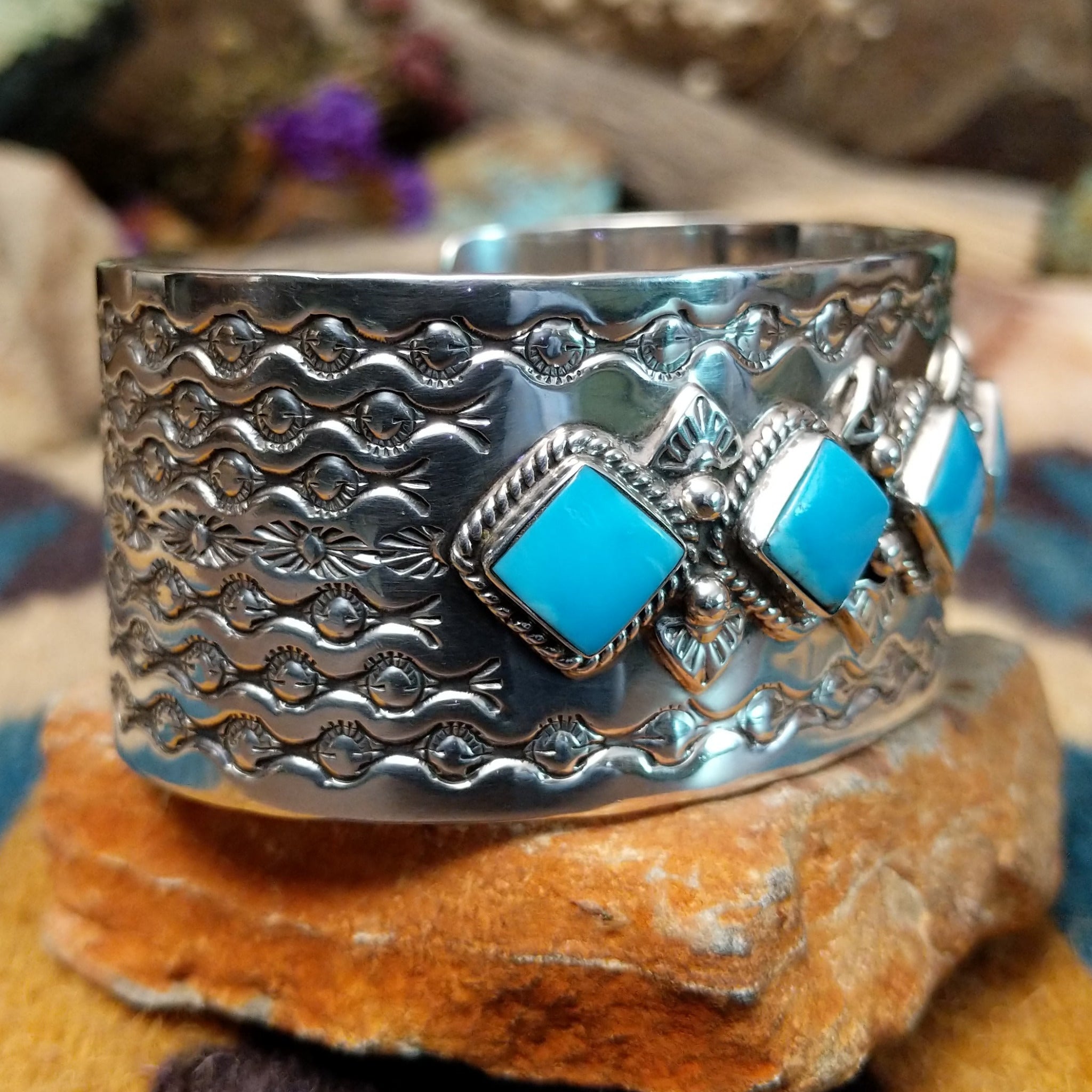 Handcrafted Navajo sterling silver cuff featuring five diamond-shaped turquoise stones in twisted rope bezels with intricate hand-stamped Southwestern designs and silver bead accents; side view.