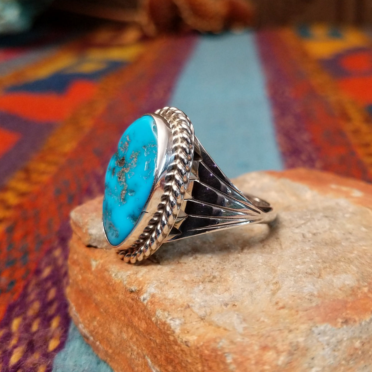 Navajo Turquoise Ring featuring a large elongated oval turquoise stone with natural brown and dark matrix, framed by twisted rope detailing and set in Sterling Silver with a split-shank band; side view.