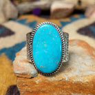 Handcrafted Navajo sterling silver ring by L.P. featuring a large oval natural turquoise cabochon with subtle golden matrix, set in a twisted rope bezel on a wide hand-stamped split-shank band.