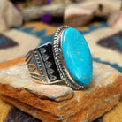 Handcrafted Navajo sterling silver ring by L.P. featuring a large oval natural turquoise cabochon with subtle golden matrix, set in a twisted rope bezel on a wide hand-stamped split-shank band; side view.