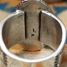 Handcrafted Navajo sterling silver ring by L.P. featuring a large oval natural turquoise cabochon with subtle golden matrix, set in a twisted rope bezel on a wide hand-stamped split-shank band; artisan stamp.