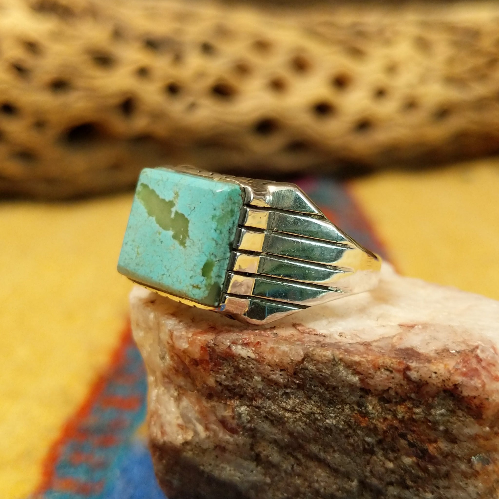 Navajo turquoise ring by R., featuring a square turquoise stone with natural blue and green tones set in a handcrafted sterling silver band with stepped side accents.  Side view.