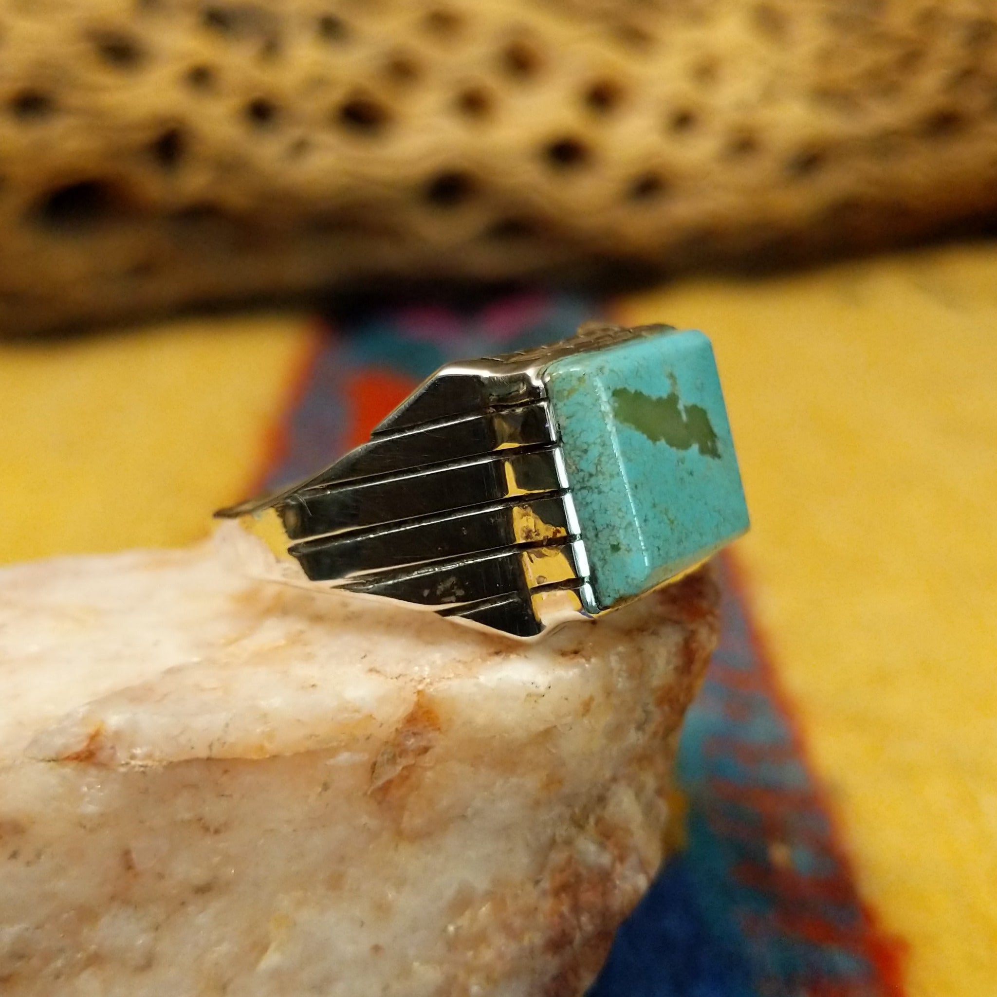 Navajo turquoise ring by R., featuring a square turquoise stone with natural blue and green tones set in a handcrafted sterling silver band with stepped side accents.  Side view.