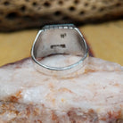 Navajo turquoise ring by R., featuring a square turquoise stone with natural blue and green tones set in a handcrafted sterling silver band with stepped side accents.  Underside view.