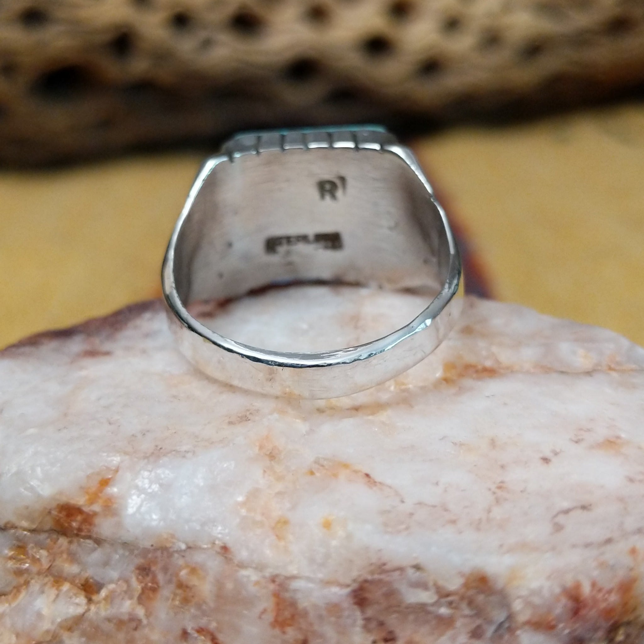 Navajo turquoise ring by R., featuring a square turquoise stone with natural blue and green tones set in a handcrafted sterling silver band with stepped side accents.  Underside view.