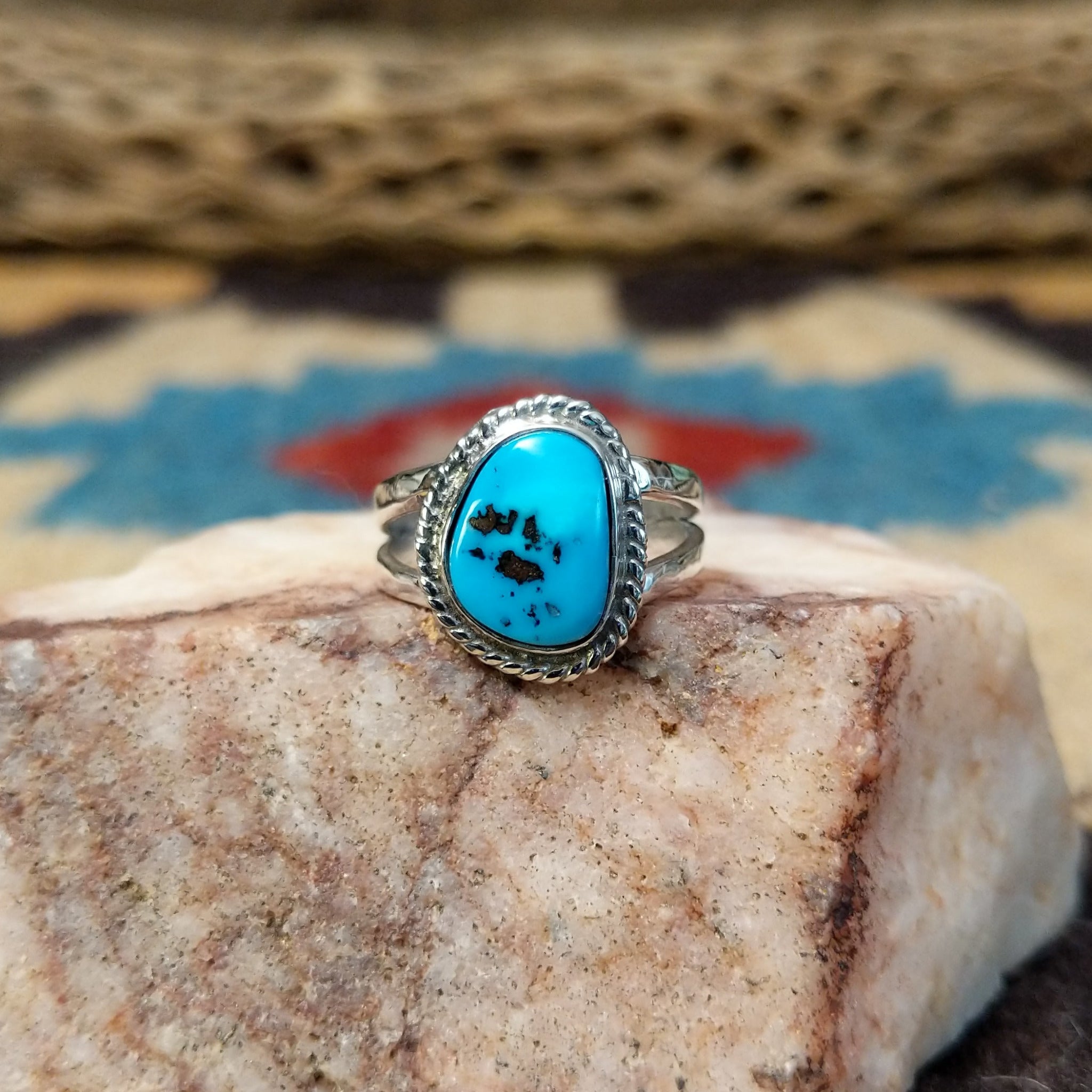 Navajo turquoise ring by S.S., featuring a vibrant blue turquoise stone with natural black matrix, surrounded by a twisted rope border and set in a handcrafted sterling silver split shank band.