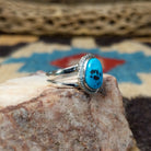 Navajo turquoise ring by S.S., featuring a vibrant blue turquoise stone with natural black matrix, surrounded by a twisted rope border and set in a handcrafted sterling silver split shank band.  Side view.