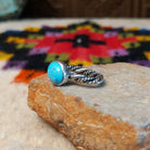 This graceful Navajo Twisting Turquoise Ring features a rounded sky-blue turquoise stone with subtle natural matrix, set in a smooth silver bezel on a twisted silver band; side view.