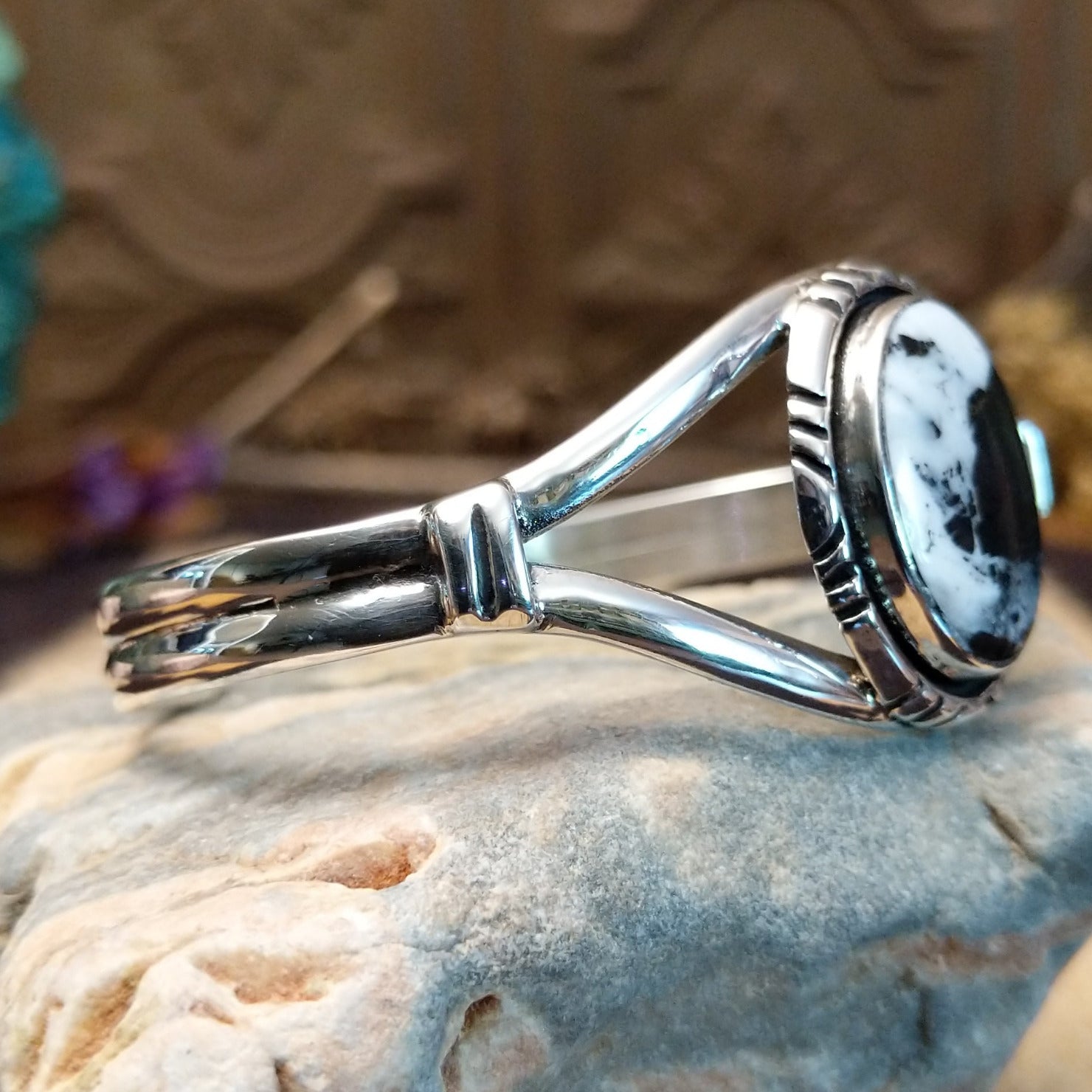 Sterling silver cuff bracelet with a white buffalo stone set in a round bezel, framed by incised lining and a layered band.