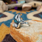 Handcrafted Navajo sterling silver ring featuring an elongated oval White Buffalo inlay with black onyx, turquoise, and sterling silver geometric accents in a polished bezel setting; side view.