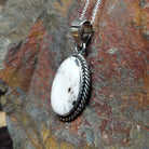 Handcrafted sterling silver Navajo White Buffalo portrait pendant by K., featuring a natural White Buffalo gemstone in a twisted rope bezel setting; side view.