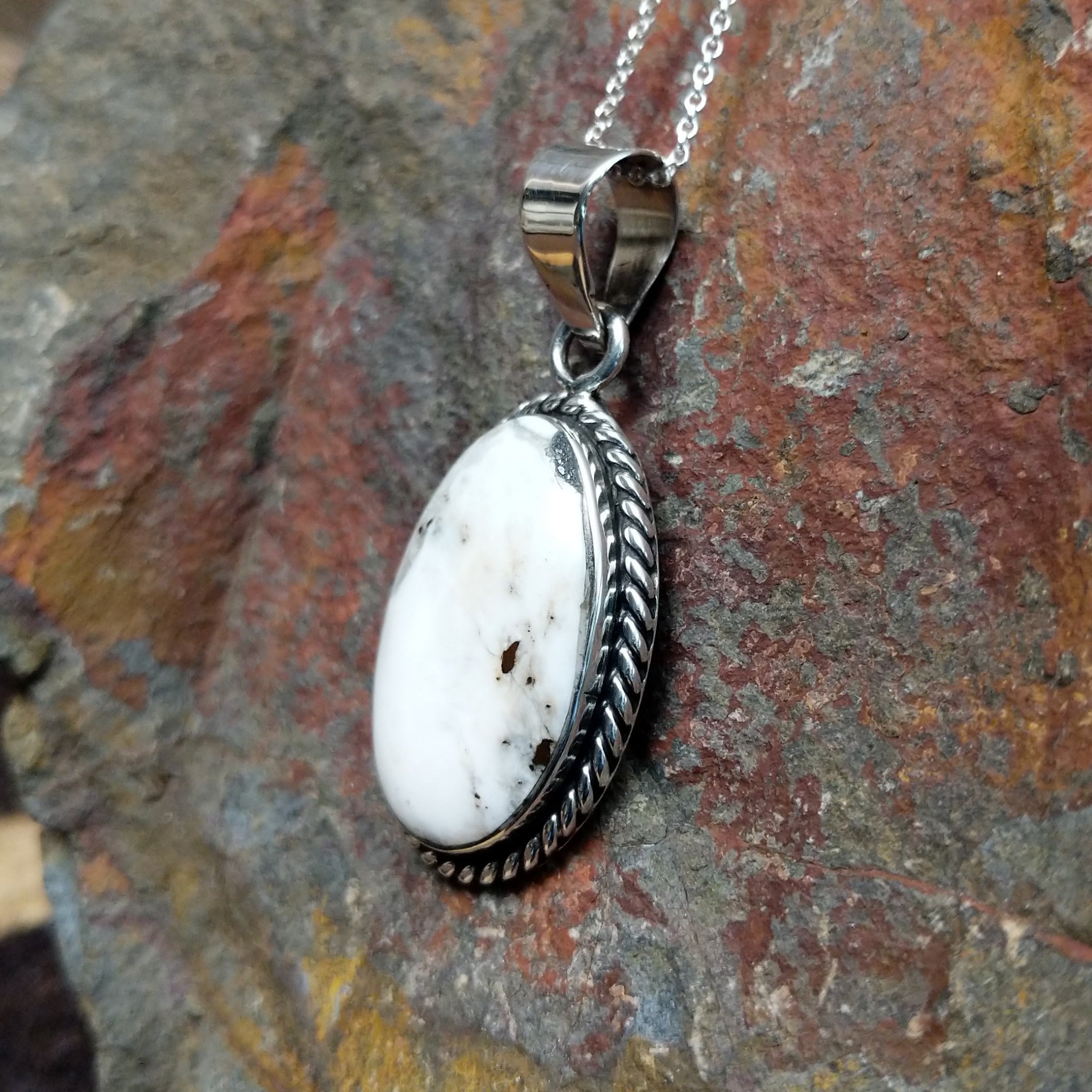 Handcrafted sterling silver Navajo White Buffalo portrait pendant by K., featuring a natural White Buffalo gemstone in a twisted rope bezel setting; side view.