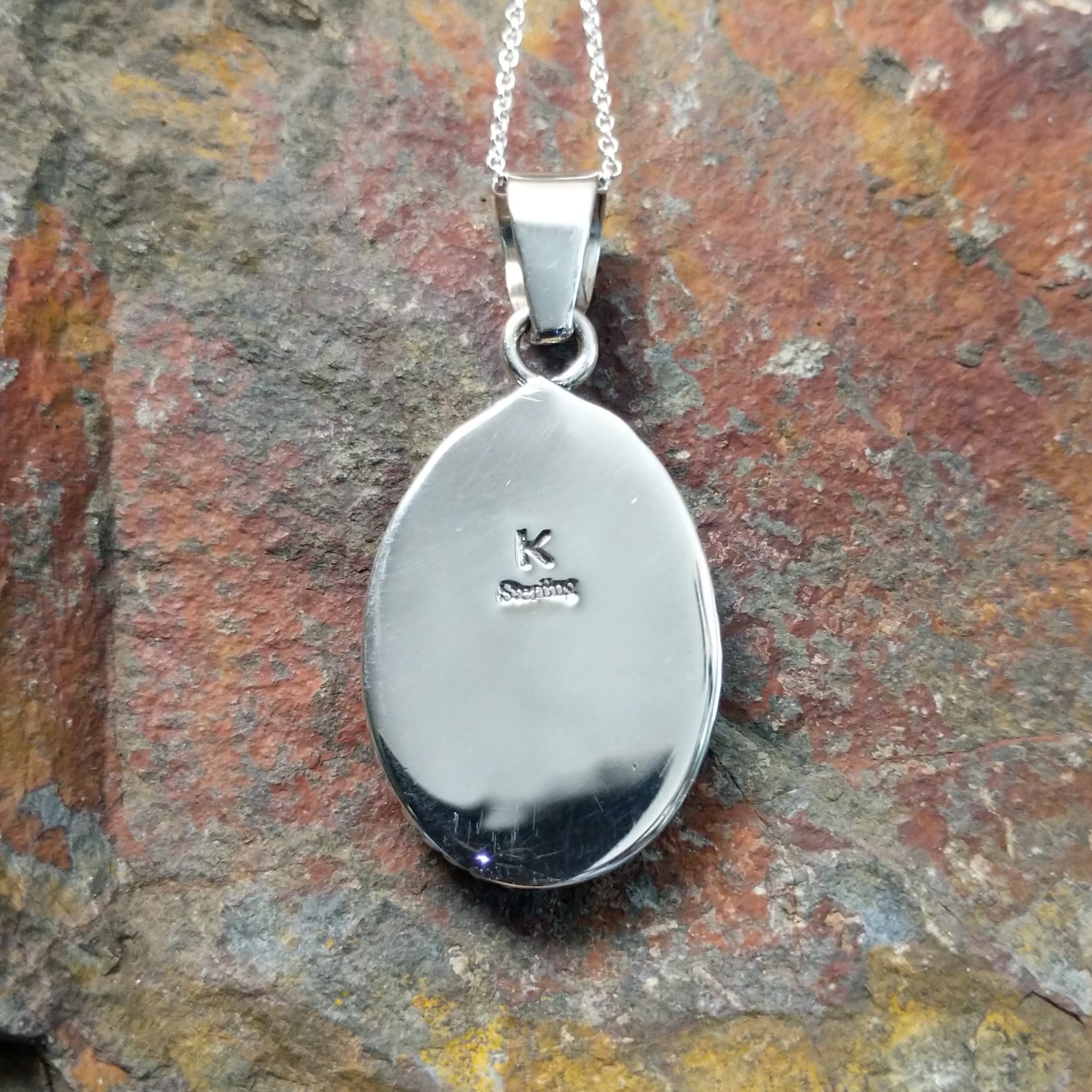 Handcrafted sterling silver Navajo White Buffalo portrait pendant by K., featuring a natural White Buffalo gemstone in a twisted rope bezel setting; artisan and Sterling Silver stamp.