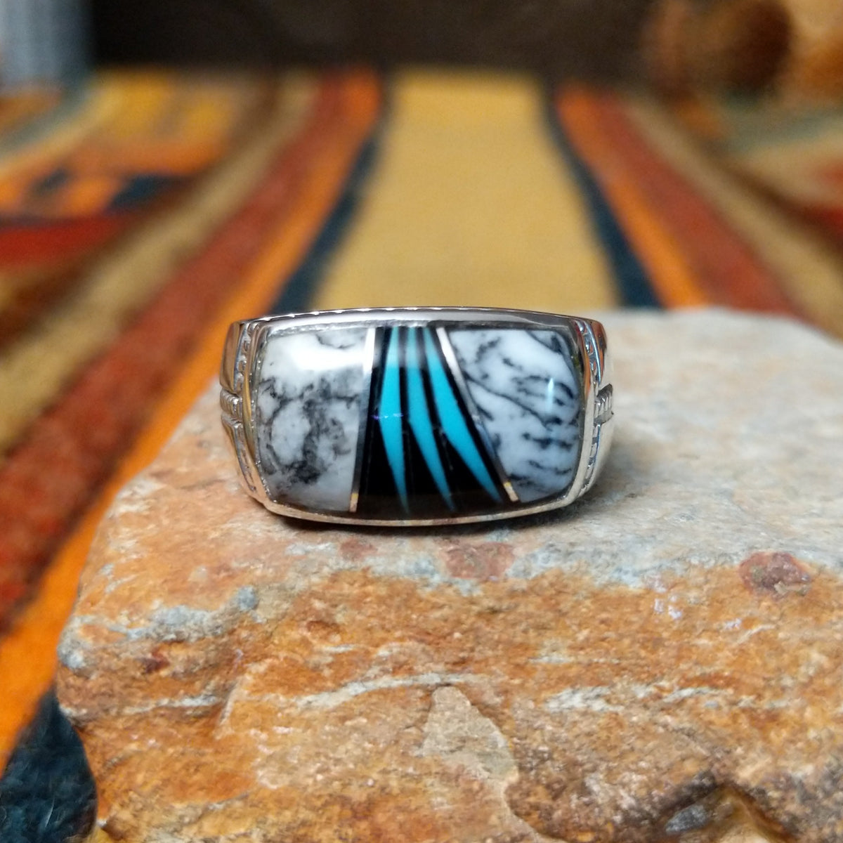 This elegant Navajo White Buffalo with Turquoise Inlay Ring features a rectangular silver setting with black-and-white White Buffalo stone and vibrant turquoise inlay arranged in a flowing geometric pattern.