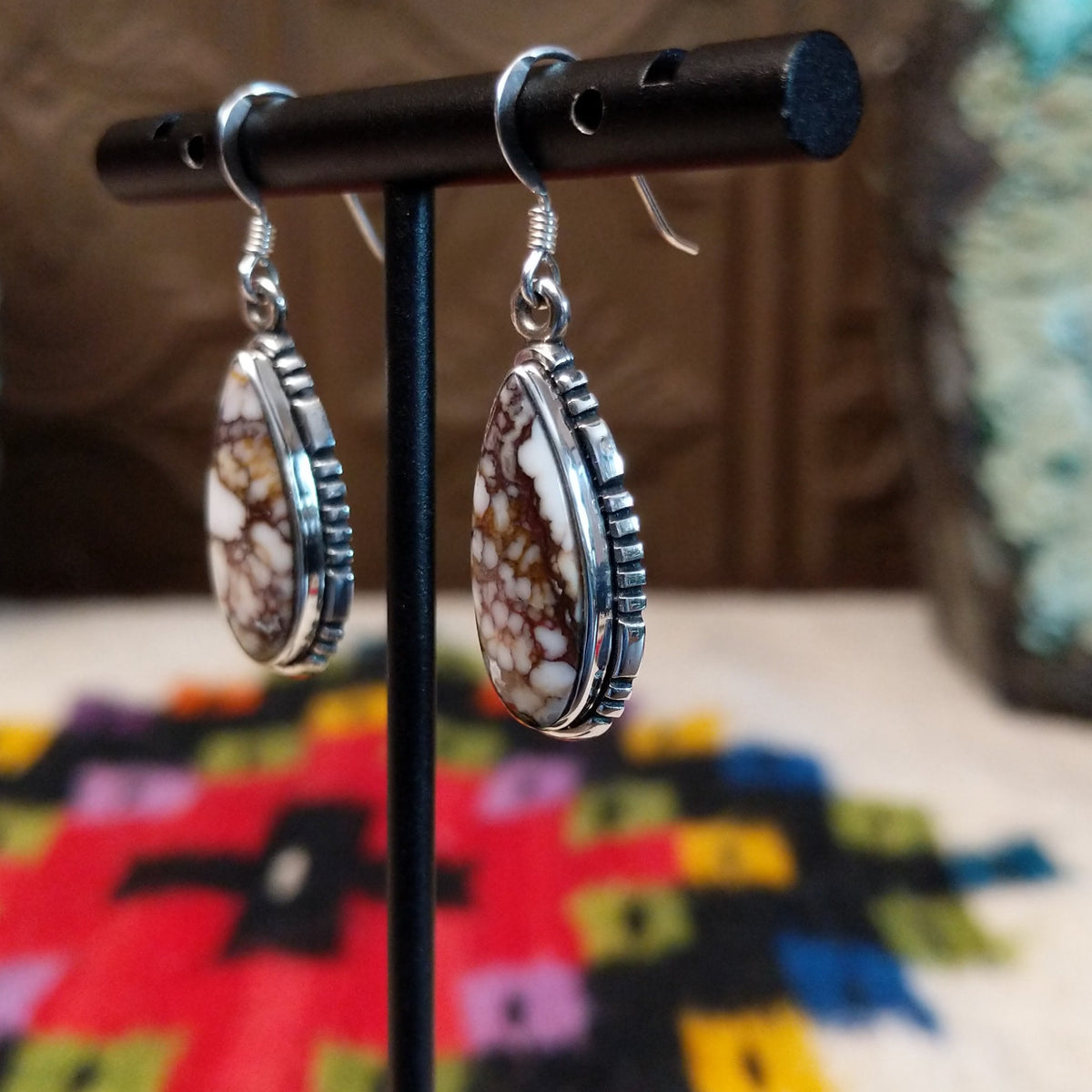 Navajo Wild Horse Teardrop Earrings by B.A. featuring polished white and reddish-brown matrix stones in detailed silver settings with French ear wires; side view.