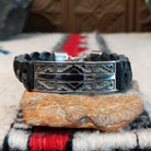 Navajo bracelet with braided black leather and a rectangular polished silver centerpiece featuring repeating stepped geometric patterns and central triangular designs.