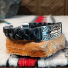 Navajo bracelet with braided black leather and a rectangular polished silver centerpiece featuring repeating stepped geometric patterns and central triangular designs; side view.