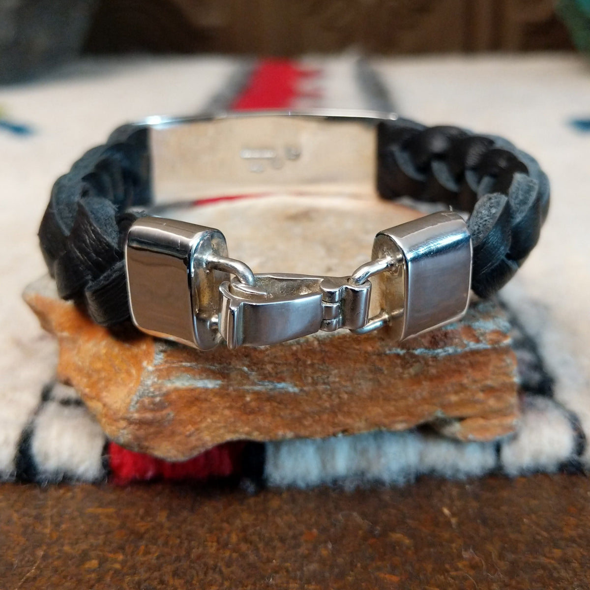Navajo bracelet with braided black leather and a rectangular polished silver centerpiece featuring repeating stepped geometric patterns and central triangular designs; clasp view.
