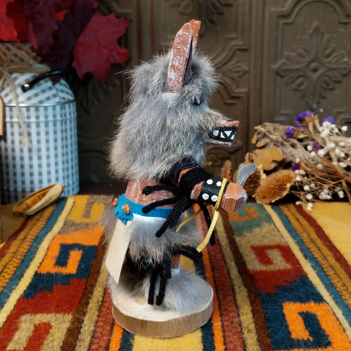 Side view of the Navajo Wolf Kachina doll with gray fur, pointed ears, painted teeth, black clothing with white spots, and feather accents.