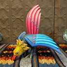 Oaxacan bird wood carving with a vibrant yellow head, orange beak, and expansive blue wings adorned with intricate patterns.