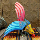 Oaxacan bird wood carving with a vibrant yellow head, orange beak, and expansive blue wings adorned with intricate patterns.