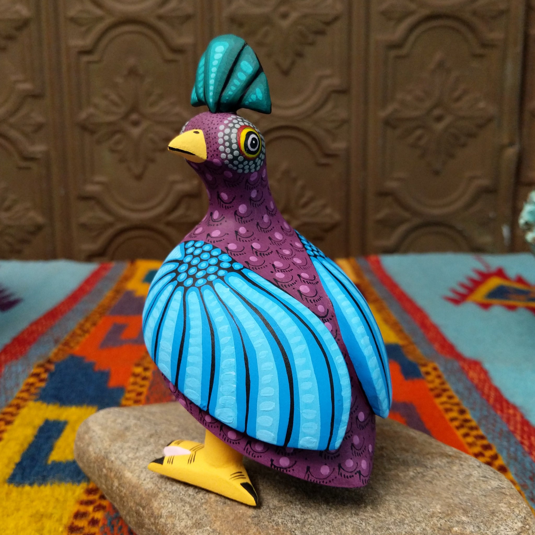 Oaxacan bird wood carving by Hedilberto Olivera with a purple body, broad blue wings, fan-shaped crest, and yellow beak and feet.