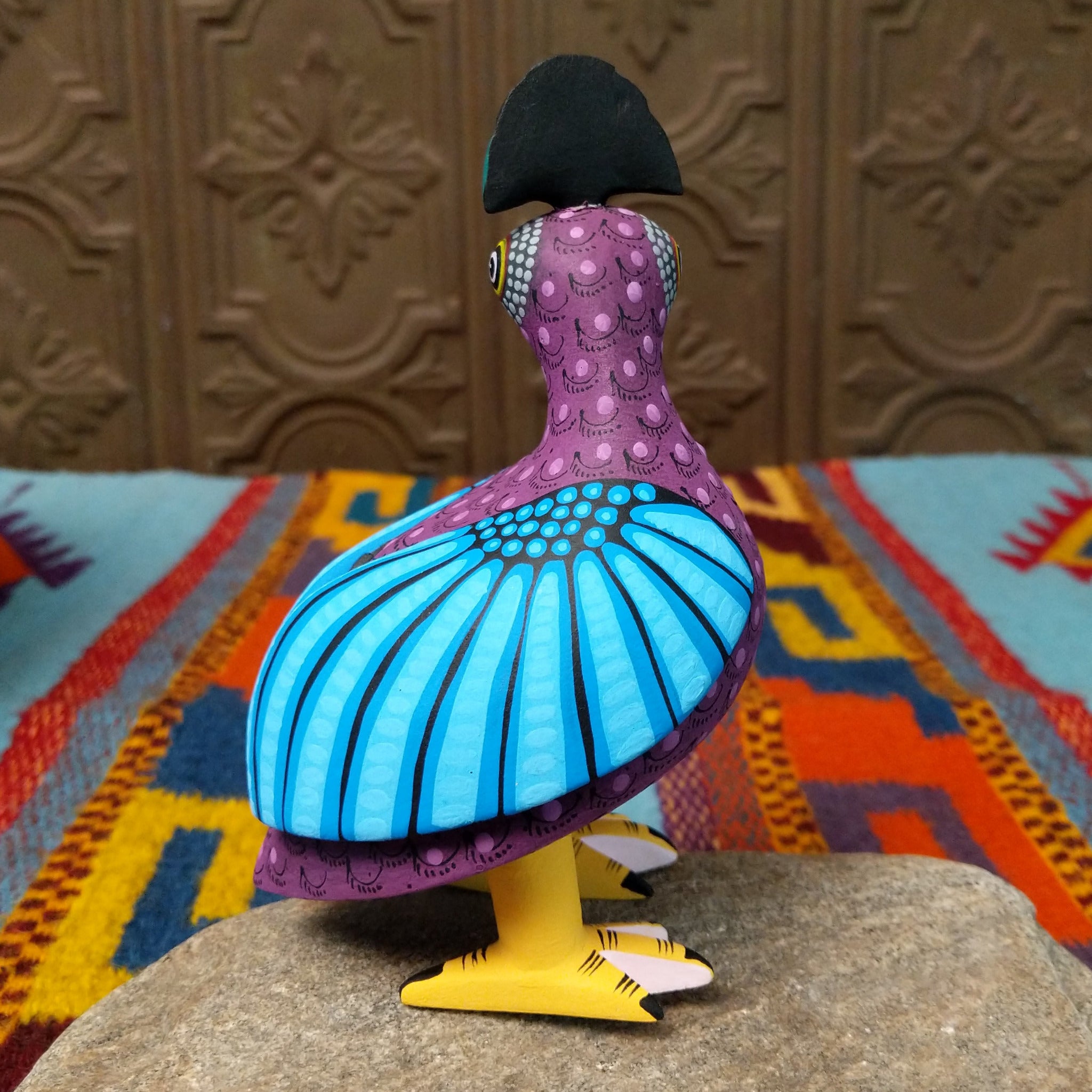Oaxacan bird wood carving by Hedilberto Olivera with a purple body, broad blue wings, fan-shaped crest, and yellow beak and feet.