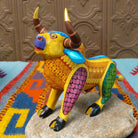 Oaxacan bull wood carving by Abundio Muñoz with curved horns, a golden yellow body, and colorful geometric patterns across the legs and torso.