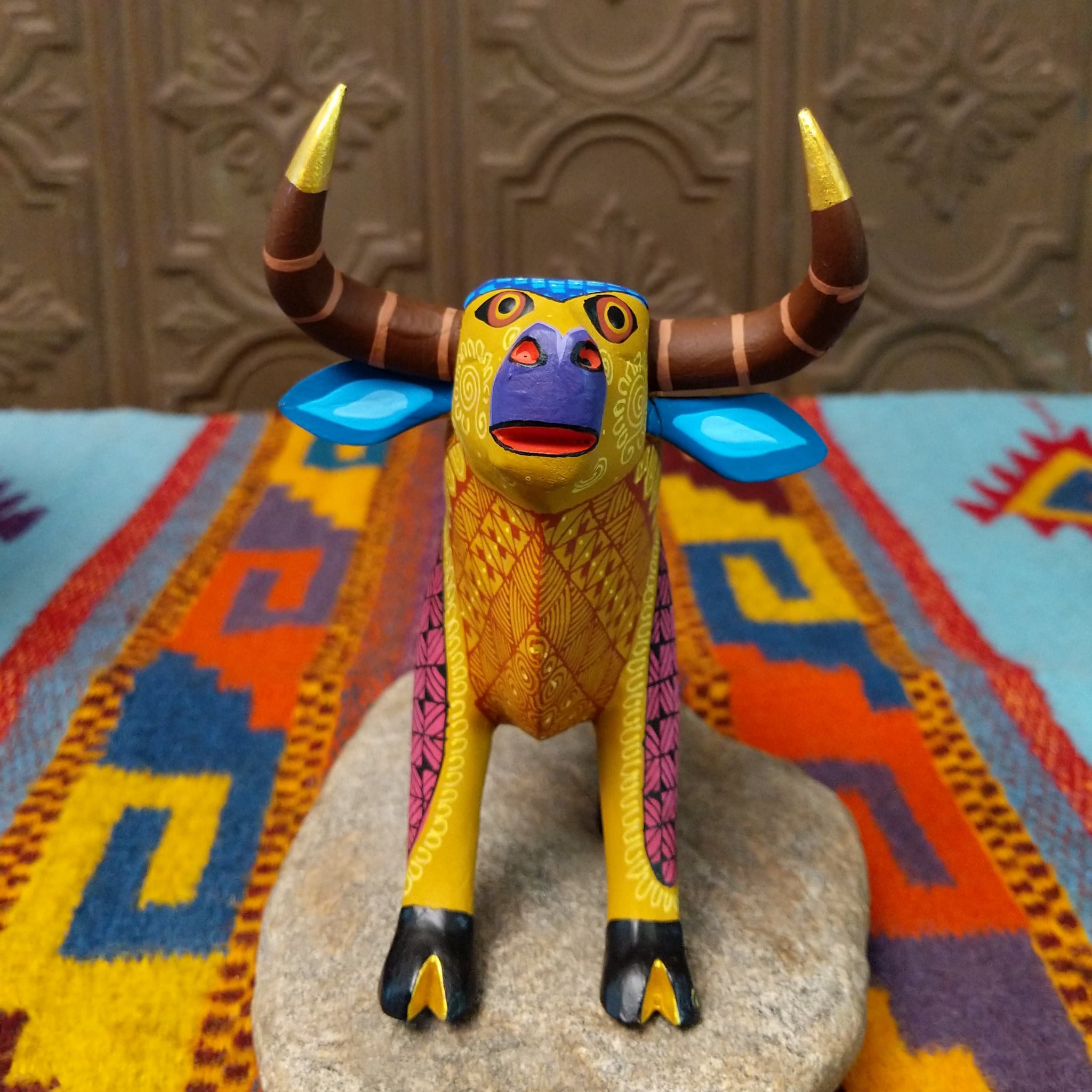 Oaxacan bull wood carving by Abundio Muñoz with curved horns, a golden yellow body, and colorful geometric patterns across the legs and torso.