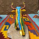 Oaxacan bull wood carving by Abundio Muñoz with curved horns, a golden yellow body, and colorful geometric patterns across the legs and torso.