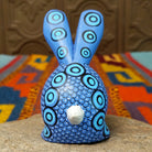 Blue Oaxacan bunny wood carving by Alberto Hernandez with tall ears, ringed eyes, and layered circular and scale-like painted patterns.